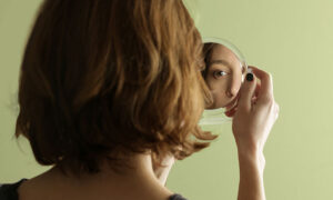 Kvinna tittar in i liten spegel och man ser bara hennes öga.