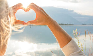 Kvinna som står i naturen vid en sjö och formar händerna till ett hjärta.