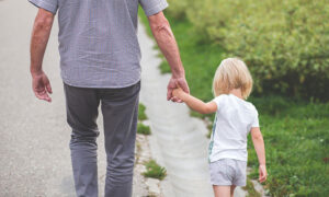 Pappa som går på promenad och håller sitt lilla barn i handen